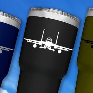 May include: Three insulated tumblers in navy blue, black, and olive green, each featuring a white jet plane graphic. The tumblers have a silver rim and white base. The text "feGraphics.com" and "CUP NOT INCLUDED" are also visible.