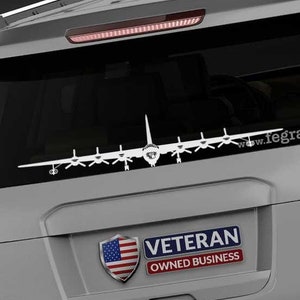 May include: A gray SUV with a white silhouette of a C-130 Hercules aircraft on the rear window. The vehicle has a "Veteran Owned Business" sticker with an American flag on the rear bumper. The text "www.fegraphics.com" is printed on the bumper.