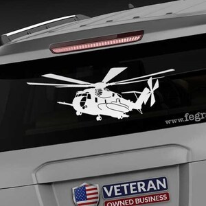 May include: A white silhouette of a helicopter on a gray car with a "Veteran Owned Business" sticker and the website "www.fegraphics.com" on the back.