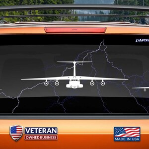 May include: White vinyl decal of a C-130 Hercules aircraft on a black car window. The decal is surrounded by a lightning bolt design. The text "LIGHTNING NOT INCLUDED" is at the top of the image. The text "www.fegraphics.com Flight Engineered Graphics Aircraft Decals" is at the bottom left of the image. The text "VETERAN OWNED BUSINESS" is at the bottom center of the image. The text "MADE IN USA" is at the bottom right of the image.