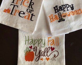 May include: Three white linen towels with Halloween and Fall themed embroidery. One towel says "Trick or Treat" with candy corn. Another says "Happy Halloween" with a pumpkin and witch legs. The third says "Happy Fall Y'all" with a pumpkin and hearts.