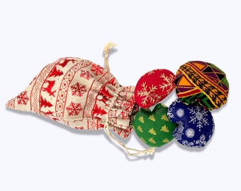 May include: A small burlap bag with a red and white reindeer and snowflake pattern, filled with four small fabric hearts. The hearts are red with gold snowflakes, green with a Christmas tree pattern, blue with a snowflake pattern, and yellow, orange, and black with a geometric pattern.