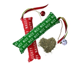 May include: Two red and green cat toys with a Christmas theme. The toys are shaped like bones and have the words "Nice" and "Naughty" printed on them. The toys are tied together with a red ribbon and a white bell.