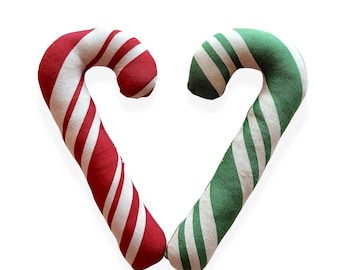 May include: Two fabric candy cane ornaments arranged in a heart shape. One candy cane features diagonal red and white stripes, while the other candy cane features diagonal green and white stripes. Both items have a soft, plush, and textured appearance.