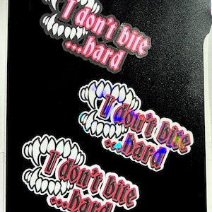 May include: Three stickers on a black background. Each sticker shows a set of white teeth with pink accents and the text "I don't bite...hard" in pink. One sticker has a holographic effect.
