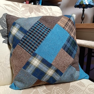 Puede incluir: Una almohada de patchwork azul y marrón con un patrón de diamante. La almohada está hecha de diferentes telas, incluyendo cuadros, espiga y pata de gallo.