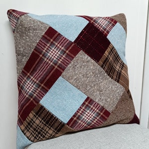 May include: A patchwork pillow with a variety of brown, blue, and red plaid fabrics. The pillow is square and has a soft, textured surface.
