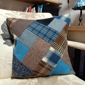 Puede incluir: Una almohada de patchwork azul y marrón con un patrón geométrico. La almohada está hecha de diferentes telas y tiene una sensación suave y cómoda.