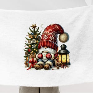 May include: A white Christmas-themed throw blanket featuring a gnome holding a mug, sitting beside a Christmas tree adorned with presents and a lantern. The gnome is wearing a red and white knitted hat with a white pom-pom. A sign hanging from the tree reads "Warm Wishes".