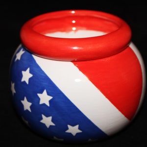 May include: A white ceramic planter with a red, white, and blue American flag design. The planter has a wide, red rim.