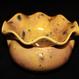 May include: A yellow ceramic planter with a ruffled top and speckled glaze. The planter has a light brown base and a yellow top with green and blue speckles.