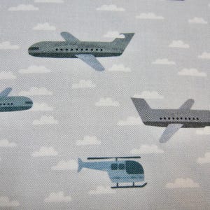 May include: A light gray fabric with a repeating pattern of airplanes, helicopters, and white clouds. The airplanes are gray with black windows and the helicopters are light blue. The clouds are white.