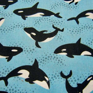 May include: A blue fabric with a repeating pattern of black orca whales. The orcas are swimming in different directions and some are jumping out of the water.