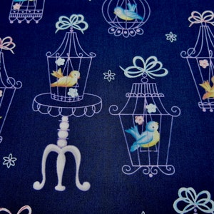 May include: Dark blue fabric with a repeating pattern of white birdcages, each with a yellow or blue bird inside. The birdcages are ornate, with bows and floral accents. Small white flowers and bows are scattered throughout the design.
