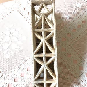 May include: A white ceramic brick with a geometric pattern of triangles and squares. The brick has a rough texture and is designed for ventilation.