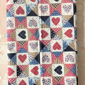 May include: A folded piece of fabric featuring a repeating quilt-style pattern of hearts and geometric shapes in shades of red, navy blue, and cream. The design consists of alternating squares with heart motifs and various small floral or striped prints.