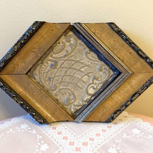 May include: An antique, diamond-shaped frame with a central, ornate panel. The frame is constructed of wood with a gold finish and dark trim. The central panel features a textured, light-colored design.