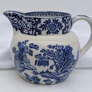 May include: A blue and white ceramic jug with a floral design and a landscape scene. The jug has a round body and a handle.