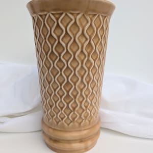 Peut inclure: Un vase en céramique brun avec un motif en diamant texturé. Le vase a une large ouverture et une base étroite.