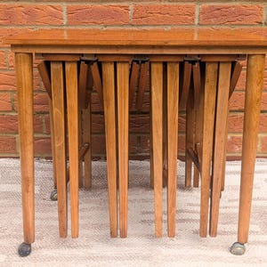 May include: A set of four wooden nesting tables in light brown. Each table has rounded legs with small wheels and a rectangular top. The tables are nested, with the smallest table inside the largest. The tables are approximately 60 cm long.