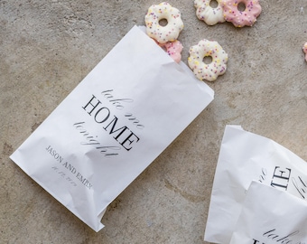 May include: Two white paper bags with the text "take me home tonight" and the names "Jason and Emen" printed on them. The bags are filled with pink and white frosted cookies.