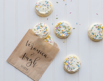 May include: A brown paper bag with the text "Veronica & Hugh 12.21.17" printed on it. The bag is filled with five frosted sugar cookies decorated with colorful sprinkles.
