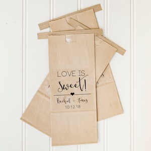 May include: Three brown paper bags with a white label on the front. The label says "Love is Sweet!" with a small heart and the text "Rachel + Thomas 10.12.18".
