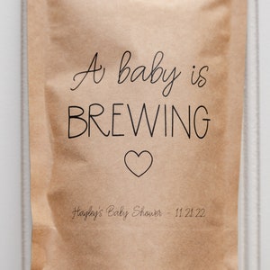 Pu&ograve; includere: Un sacchetto di carta marrone con il testo "A baby is BREWING" e un cuore. Il sacchetto ha anche il testo "Hayley's Baby Shower - 11.21.22".