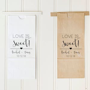 May include: Two white and brown paper bags with a black and white design that says "Love is Sweet!" with the names Rachel and Timos and the date 10.12.18 printed on them.