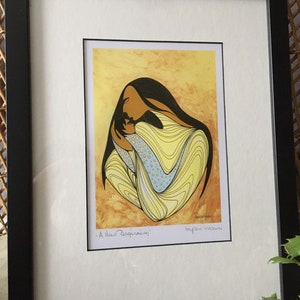 May include: A framed print of a Native American art piece depicting a mother and child. The mother is holding the child close, and both are surrounded by yellow and blue swirls. The title of the piece is "A New Beginning" and is signed by the artist, "Joya Mani".