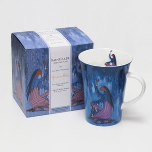 Pode incluir: Uma caneca de cerâmica azul e uma caixa a condizer com um design nativo americano. A caneca e a caixa retratam uma figura com uma túnica azul e cabelo comprido, estendendo-se para a chuva que cai. O texto na caixa diz "Rainmaker" e "Rain drops provide life on Earth."