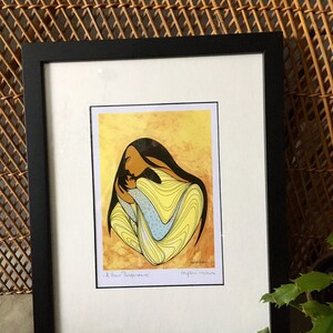 May include: A framed print of a colorful abstract painting depicting a woman holding a child. The painting is in yellow, blue, and white tones. The title of the painting is "A New Beginning" and the artist's signature is "Leyla Moos"