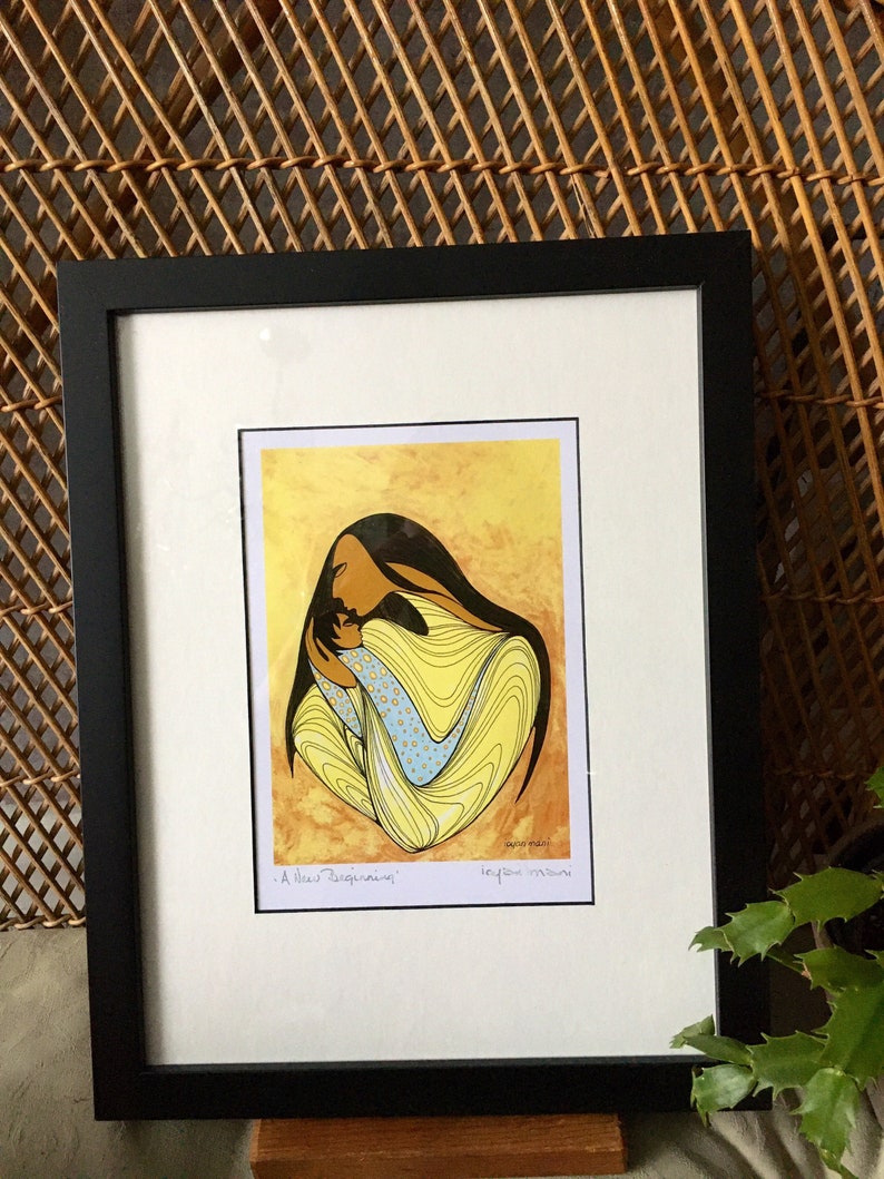 May include: A framed print of a colorful abstract painting depicting a woman holding a child. The painting is in yellow, blue, and white tones. The title of the painting is "A New Beginning" and the artist's signature is "Leyla Moos"