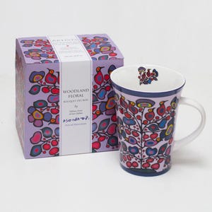 Pode incluir: Uma caneca de cerâmica branca com um design floral colorido. A caneca apresenta uma árvore estilizada com flores vermelhas, azuis, amarelas e roxas. A caneca é embalada em uma caixa com o mesmo design. A caixa também inclui o nome do artista, "Asanda", e o título da obra de arte, "Woodland Floral".