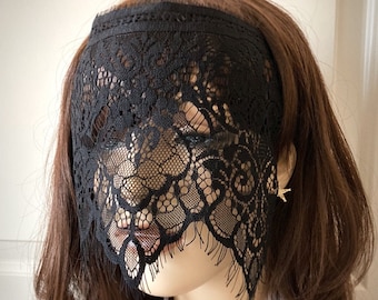 May include: Black lace mask with a scalloped edge. The mask covers the eyes and nose, leaving the mouth visible. The lace is delicate and intricate, with a floral pattern.