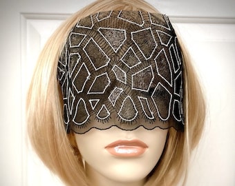 May include: Black lace eye mask with a geometric pattern and silver thread embroidery. The mask has a scalloped edge.
