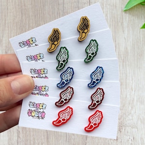May include: A collection of wing-shaped stud earrings in various colors, including wood grain, green glitter, blue glitter, and red glitter. The earrings are displayed on white cards with the text "LASER COLOR DESIGNS".