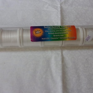 May include: A clear plastic tube containing six spools of white SolarActive thread. The label reads "SolarActive Thread Changes Color in the Sunlight.  Visible:  Pink, Orange, Green, Blue, Violet, White. No bleach, do not iron, do not dry clean.  Dispose of safely.  Made in USA.  SolarActive.  International Patent Pending."