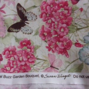 May include: A white fabric with a floral pattern featuring pink and blue flowers and butterflies. The fabric has the text "CP56223 Botanical Buzz Garden Bouquet, ©Susan Winget Do not use for children's sleepwear" printed on it.
