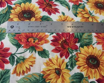 May include: White fabric with a repeating pattern of red and yellow sunflowers. A ruler is placed on top of the fabric to show the scale.