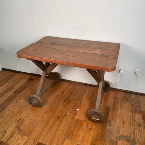 May include: A wooden table with a brown top and a dark brown base. The table has four wheels and is made of wood.