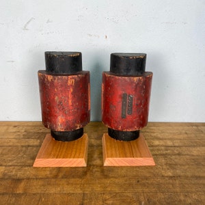 May include: Two vintage wooden shoe forms with black tops and red bases. The bases are on small wooden blocks. The forms are labeled "WILCOX & CO.  CHICAGO."