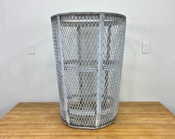 May include: A silver metal trash can with a wire mesh design. The can has a round top and a cylindrical shape.