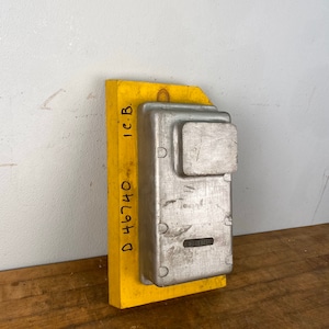 May include: A yellow wooden block with a metal mold attached to it. The mold has a rectangular shape with a smaller square cutout in the center. The block has the text "D 46740 1C.B." written on it.
