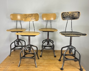 Könnte beinhalten: Vier vintage industrielle Metallstühle mit verstellbarer Höhe und gelben gepolsterten Sitzen. Die Stühle sind in einer Reihe auf einer Holzoberfläche angeordnet.