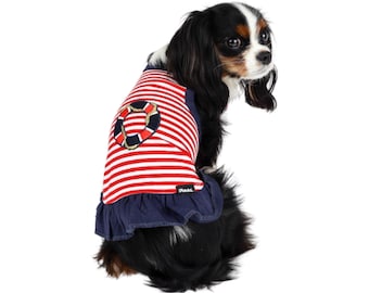May include: A small dog wearing a red and white striped dress with a blue ruffle and a life preserver graphic. The dress has the word "Chulo" on the bottom.