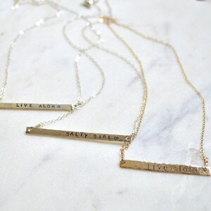 May include: Three silver necklaces with hammered bar pendants. The pendants are engraved with the phrases "Live Aloha", "Salty Girl", and "Live Aloha".