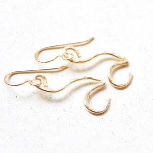 May include: A pair of gold-toned earrings with a hammered texture and a wavy, abstract design. The earrings are made of wire and have a hook closure.