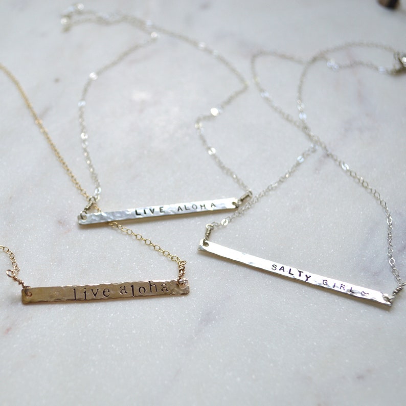 May include: Three silver necklaces with hammered bar pendants. The pendants are engraved with the phrases "Live Aloha", "Live Aloha", and "Salty Girl".