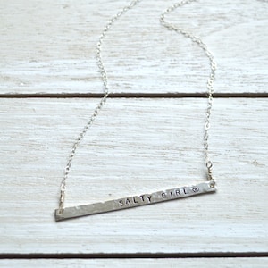 May include: A silver necklace with a hammered bar pendant that says "Salty Girl" with a heart symbol.